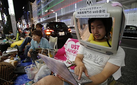  Một người đội chiếc vỏ iMac cũ ngồi đợi iPhone mới bán ra tại cửa hàng Apple ở Tokyo, Nhật Bản