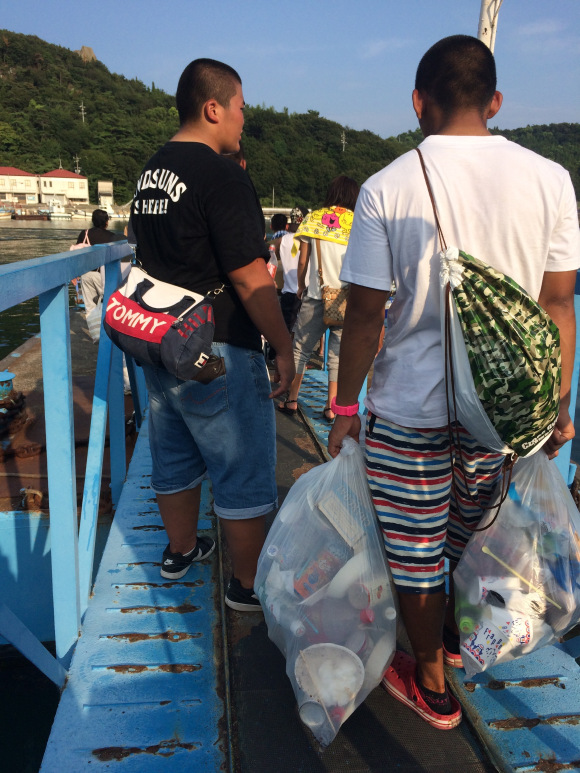 Hai người đàn ông mang túi rác của mình về sau bữa tiệc barbecue trên bãi biển Shiraishi.
