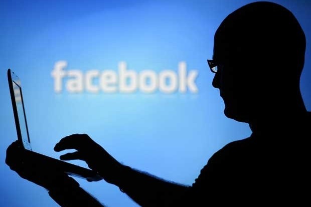 A man is silhouetted against a video screen with a Facebook logo