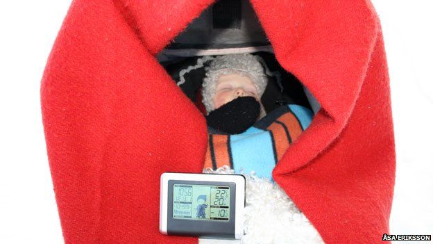  Một đứa trẻ ngủ trong xe nôi ngoài trời có gắn nhiệt kế điện tử trong thời tiết xuống tới -10°C. 