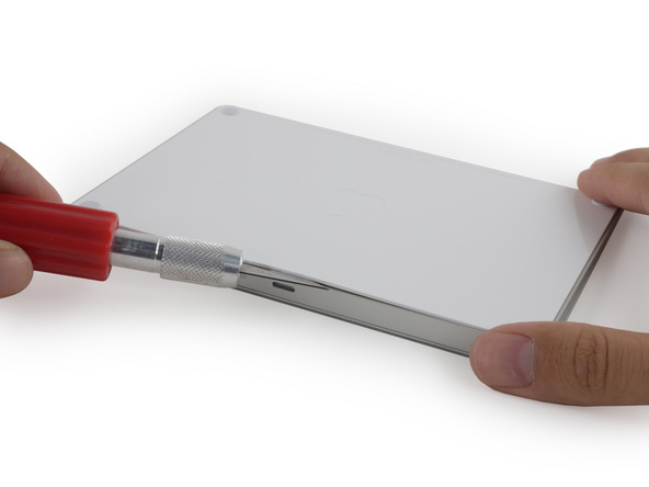  Bắt đầu mổ xẻ Magic Trackpad 2. Không hề có một con ốc nào, các kĩ sử phải hơ nóng để làm bong lớp keo liên kết bề mặt cảm ứng và đáy thiết bị. Sau khi lớp keo này bong, các miếng nhựa mỏng sẽ bắt đầu tách bàn rê ra 