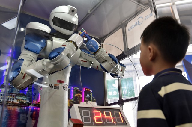  Một cậu bé đứng nhìn một chú robot đang giải khối rubic tại Triển lãm quốc tế Interet Plus Exposition ở Phật Sơn, Quảng Đông, Trung Quốc. 
