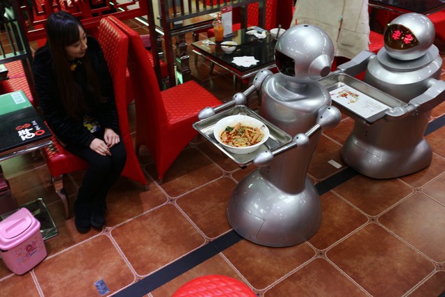  Mười robot bồi bàn phục vụ ở một nhà hàng tại Thành Đô, Trung Quốc, đang mang những món ăn đến bàn khách hàng và nói các câu mời chào đơn giản. 