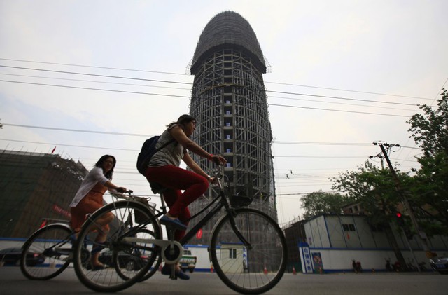 Ảnh chụp cảnh người d&acirc;n đang đạp xe đạp qua khu nh&agrave; văn ph&ograve;ng đang x&acirc;y dở của t&ograve;a b&aacute;o Nh&acirc;n d&acirc;n Trung Quốc (People's Daily) tại Bắc Kinh. Ph&aacute;c thảo của t&ograve;a nh&agrave; tr&ocirc;ng giống h&igrave;nh 