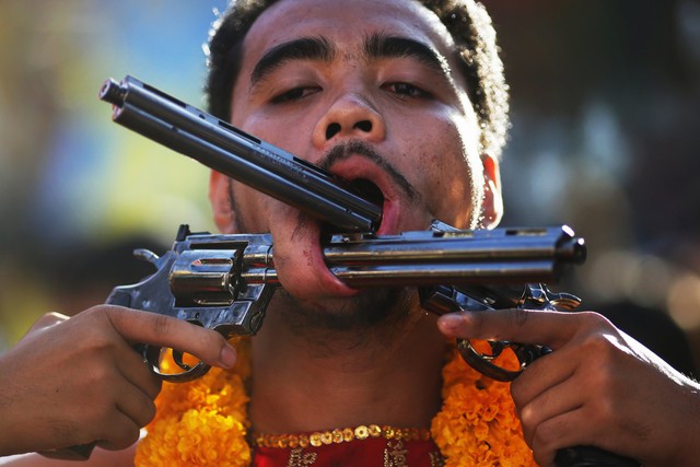 Một người đ&agrave;n &ocirc;ng với hai khẩu s&uacute;ng ngắn xuy&ecirc;n qua m&aacute; đang tham gia v&agrave;o một cuộc diễu h&agrave;nh đường phố trong lễ hội ăn chay h&agrave;ng năm ở Phuket, Th&aacute;i Lan. Ảnh chụp ng&agrave;y 10/10/2013.