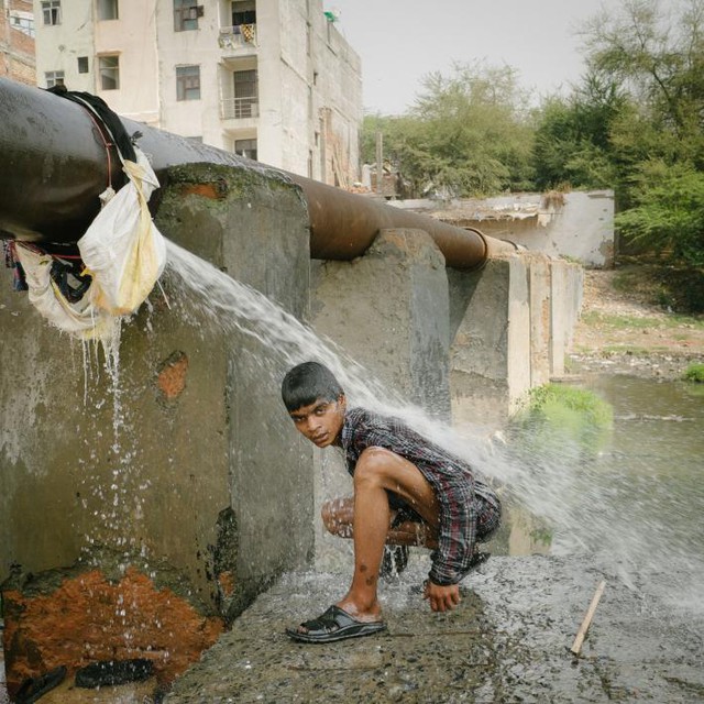  Một người bán ve chai đang rửa mình bên một cống thoát nước, nơi anh vẫn hàng ngày lùng bới đồ kiếm sống 