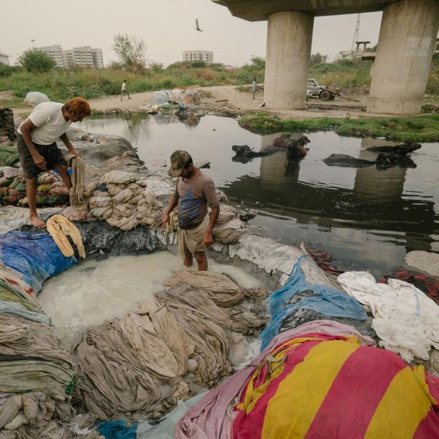  Những người đàn ông đang tẩy trắng quần áo trước khi đem xả lại chúng dưới con sông Yamuna ô nhiễm 