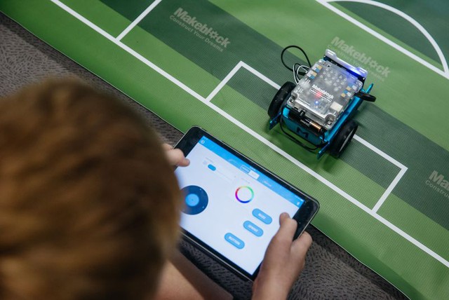 Một em học sinh dùng tablet để điều khiển robot