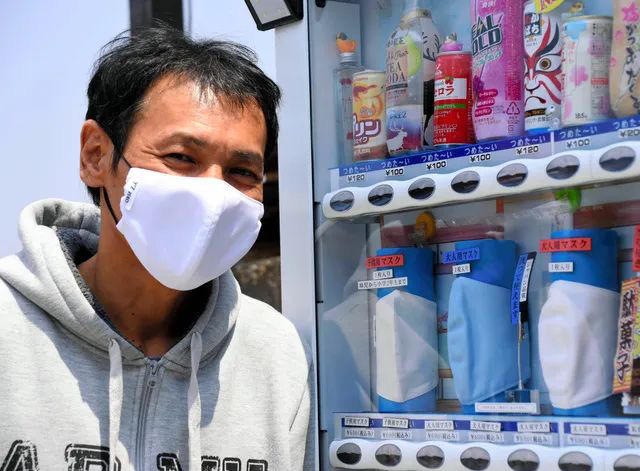 Goto đứng trước máy bán hàng tự động cùng loại khẩu trang đóng băng của mình.