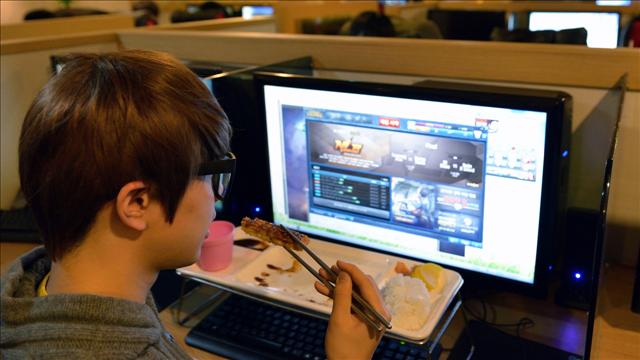 
Hình ảnh một người trẻ Hàn Quốc vừa ăn nhưng vẫn tập trung chơi Liên Minh Huyền Thoại trong quán Net
