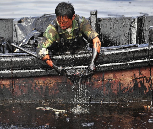 Người công nhân đang cố gắng vớt dầu bị tràn gần cảng Đại Liên thuộc tỉnh Liêu Ninh, Trung Quốc, chín ngày sau tai nạn vỡ đường ống dẫn dầu khiến 1.500 mét khối dầu thô rò rỉ xuống nước. Bức ảnh được chụp vào 26/7/2010.
