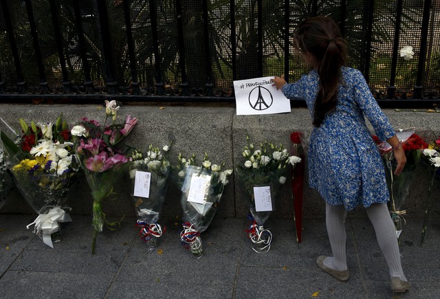  Bé gái đặt bức hình có logo do Jullien sáng tác bên cạnh những ngọn nến và vòng hoa tưởng niệm các nạn nhân của vụ khủng bố bên ngoài Đại sứ quán Pháp tại Madrid, Tây Ban Nha. 