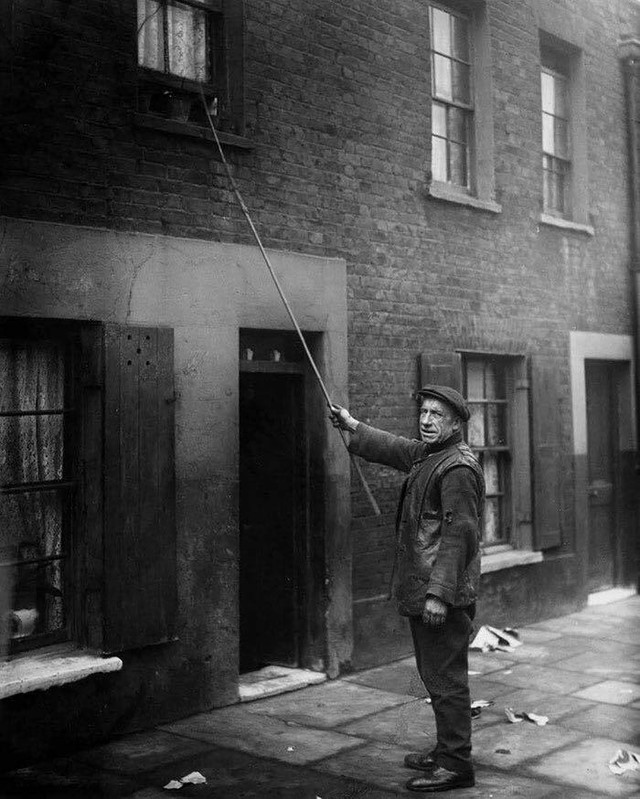 Một người làm nghề 'Knocker-Up' ở London, năm 1929. Trước khi có đồng hồ báo thức, có những người sẽ được trả tiền để đánh thức khách hàng của họ đi làm, bằng cách gõ vào cửa hay cửa sổ nhà họ bằng một cây gậy.