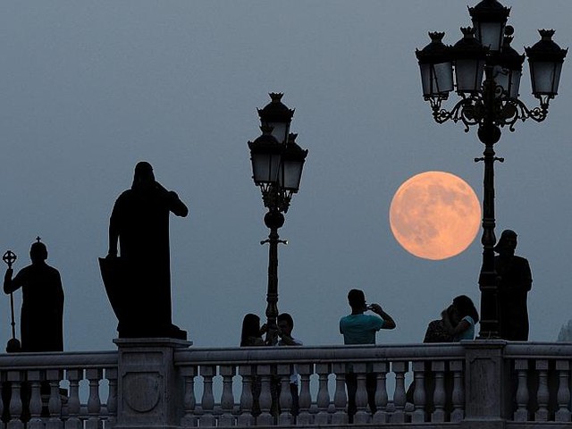 People take photos as the moon rises above a bridge over Vardar River in Skopje, Macedoni