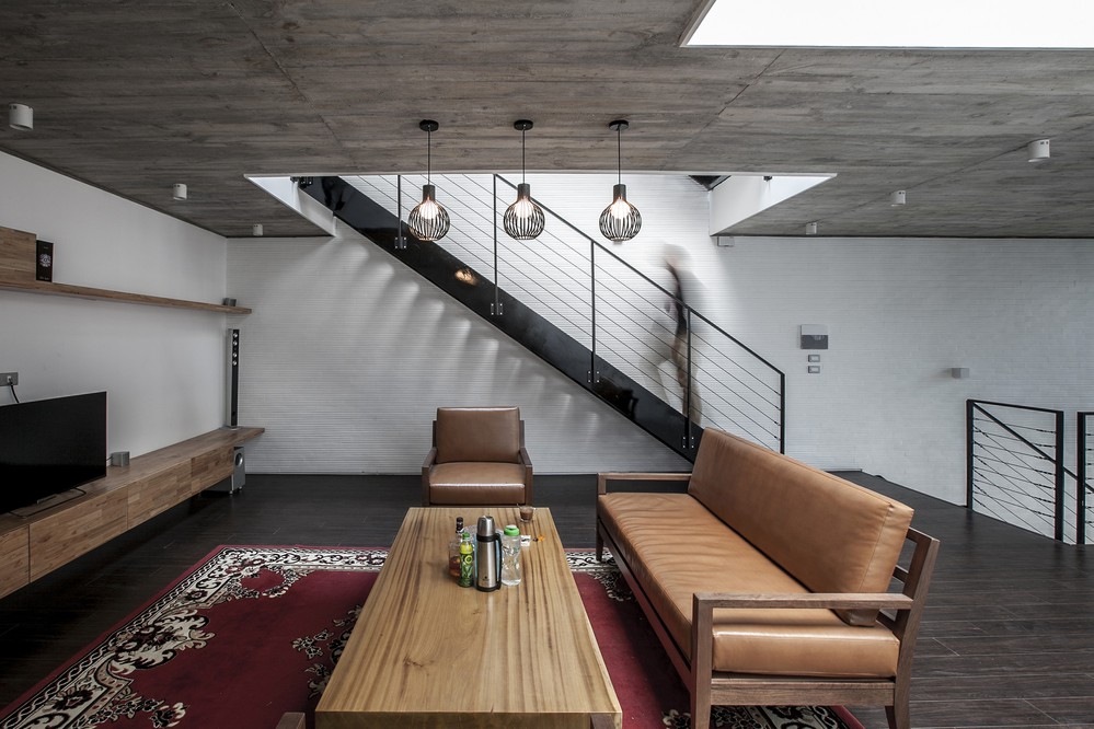  Phòng khách với bê tông trần, lát sàn gỗ màu trầm. Không gian được níu kéo bởi bộ đồ nội thất bằng gỗ và tấm thảm với tone màu nóng. 
